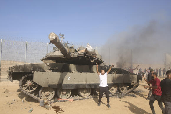 Des Palestiniens devant un char israélien en feu à la barrière frontalière de la bande de Gaza, le samedi 7 octobre 2023.