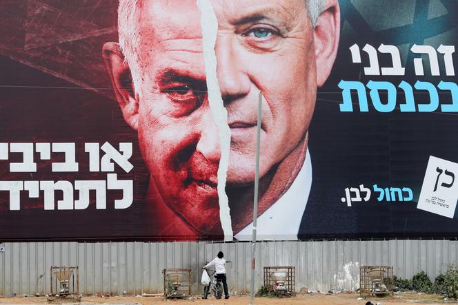 A boy looks up at an election campaign banner depicting Israeli Defence Minister Benny Gantz, alongside Israeli Prime Minister Benjamin Netanyahu, in Bnei Brak, Israel March 22, 2021. 