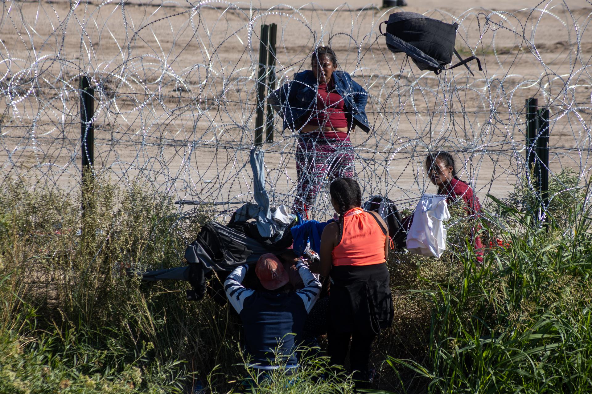 Migrants attempt to enter by crawling under barbed wire at the Mexico-U.S. border, using clothing to minimize the risk of injury, in Ciudad Juarez, Mexico, October 4, 2023.