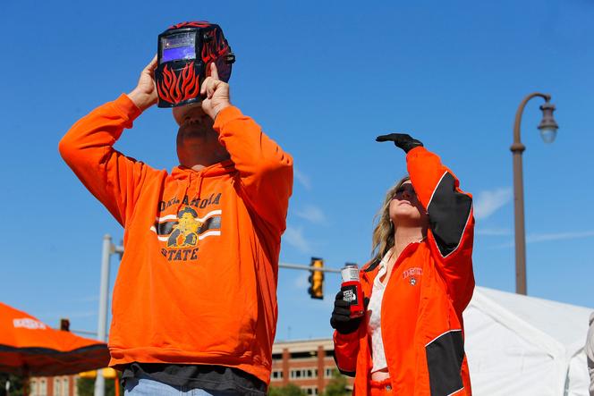 Oklahoma State Cowboys fans watch the solar eclipse through a welding helmet before a game against the Kansas Jayhawks at Boone Pickens Stadium on October 14, 2023 in Stillwater, Oklahoma.