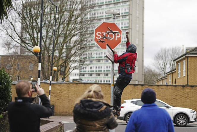 Un hombre retira una obra de arte de Banksy apenas reclamada y desvelada de la intersección de Southampton Way y Commercial Way en Peckham, sureste de Londres, el 22 de diciembre de 2023, frente a testigos que filman la escena. 