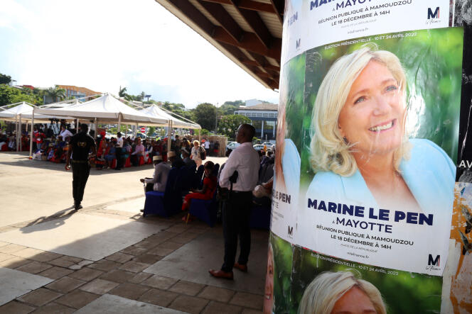 Des partisans sont assis à côté d'une affiche de la candidate du Rassemblement national à l'élection présidentielle de 2022, Marine Le Pen, lors d'une visite de campagne place Mamoudzou à Mayotte, le 18 décembre 2021.