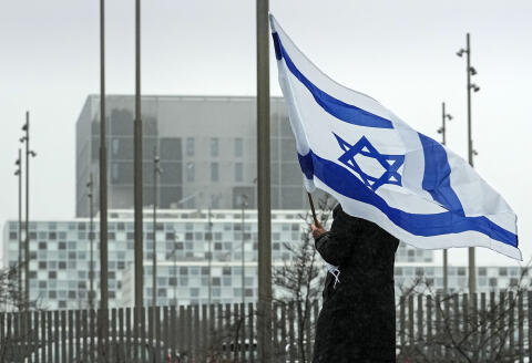 A woman holds an Israeli flag in front of International Criminal Court at The Hague, Netherlands, before a demonstration of representatives of families of hostages from the Oct. 7 cross-border attack by Hamas on Israel, Wednesday, Feb. 14, 2024. The Hostages Families Forum together with the Raoul Wallenberg Center for Human Rights want to submit a comprehensive complaint to the International Criminal Court on behalf of released hostages and families of hostages, including the issuance of arrest warrants for Hamas leaders on war crimes allegations including taking hostages, enforced disappearances, sexual violence and torture. (AP Photo/Martin Meissner)