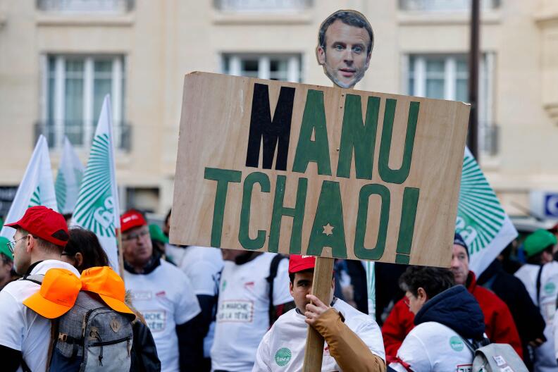 A protester holds a placard depicting French President Emmanuel Macron and reading "Ciao Manu (for Emmanuel)" in reference to the singer of the French band Mano Negra, as farmers gather at the metro station Sevres-Lecourbe in the center of Paris on February 23, 2024, amid a demonstration of French farmers called by National Federation of Farmers' Unions (FNSEA) and farmers' union Jeunes Agriculteurs (JA). Demonstrations take place across Europe with farmers demanding lower fuel taxes, better prices for products and an easing of EU environmental regulations, as in France, an agricultural fair (Salon de l'Agriculture) is to be held for its 60th edition at the Porte de Versailles exhibition centre in Paris from February 24 to March 3, 202. (Photo by Ludovic MARIN / AFP)