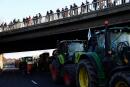 Pedestrians standing on a bridge look at French farmer tractors arriving near Chilly-Mazarin, south of Paris, on January 31, 2024 as French farmers maintain roadblocks on key highways into Paris for a third day, as part of nationwide protests called by several farmers' unions over pay, tax and regulations. Convoys of tractors edged closer to Paris, Lyon and other strategic locations in France on January 31, as thousands of protesting farmers appeared to ignore warnings of police intervention if they cross red lines laid down by the government. Farmers' unions, unimpressed by concessions offered by President Emmanuel Macron's government, encouraged their members to fight on for improved pay, less red tape and protection from foreign competition. (Photo by Emmanuel Dunand / AFP)