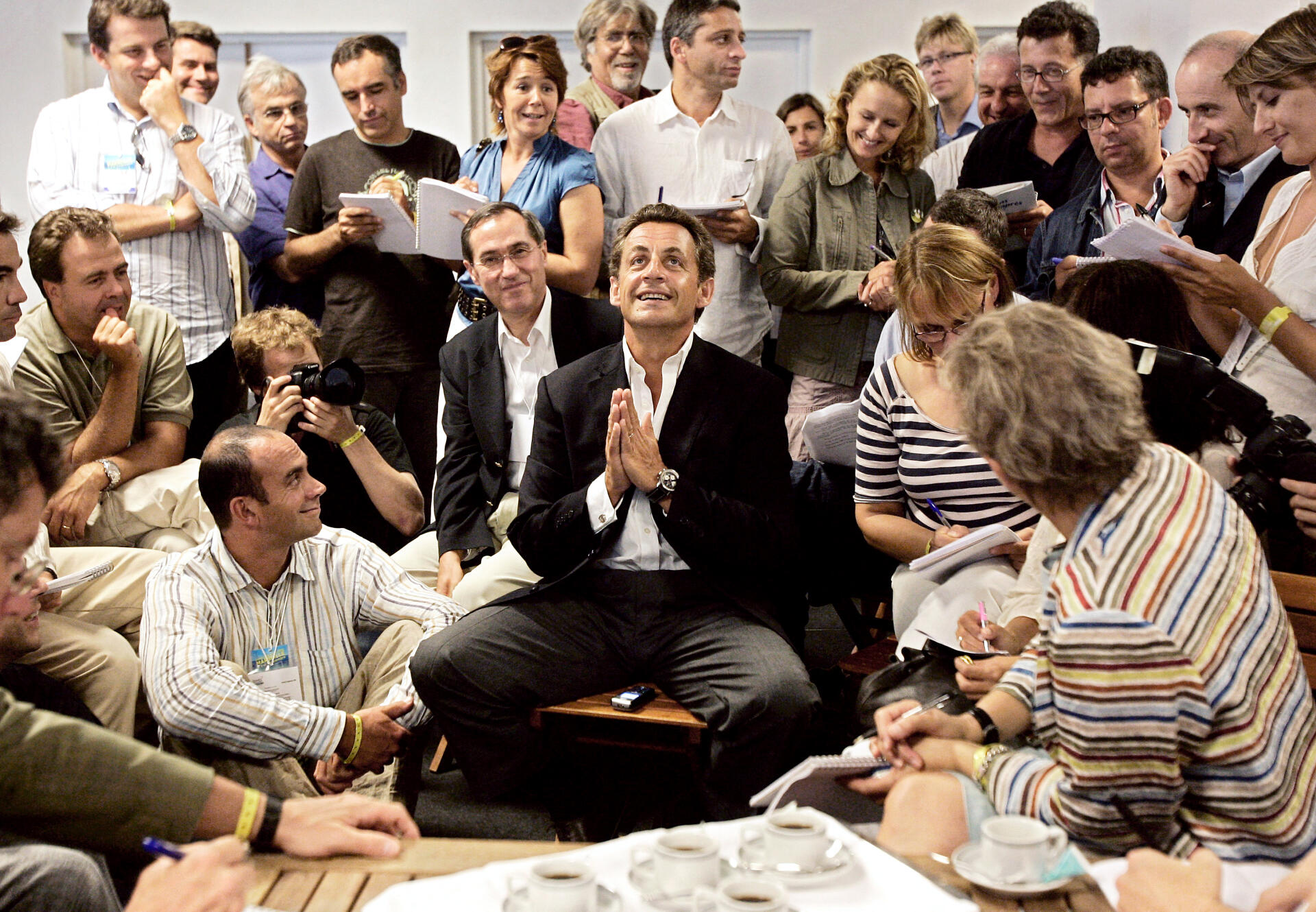 Nicolas Sarkozy, ministre de l’intérieur et candidat UMP à la présidentielle, s’adresse aux journalistes, dont deux du « Monde », Philippe Ridet (debout, 4ᵉ à dr.) et Arnaud Leparmentier (derrière lui, en chemise bleue, à lunettes), à Marseille, le 2 septembre 2006. Sont également présents Hélène Jouan (France Inter, debout, en bleu), Jean-Francois Achilli (France Inter, au centre, juste derrière Nicolas Sarkozy), Caroline Roux (Canal+, en kaki), Frédéric Haziza (LCP et Radio J, debout, 3ᵉ à droite), Géraldine Woessner (BFM-TV, debout, tout à droite), Nadège Puljak (AFP, assise à gauche de Nicolas Sarkozy), Bruno Jeudy (JDD, debout, 4ᵉ à gauche), Claude Guéant (le directeur de campagne de Nicolas Sarkozy, assis à sa droite), Luc Chatel (le porte-parole du candidat UMP, assis à gauche, la main sur la bouche).