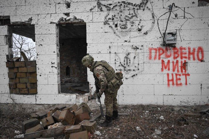 Un officier russe inspecte une zone à la recherche d’engins explosifs. Sur le mur, écrit en ukrainien, « vérification de mine faite ». A Avdïivka, le 22 mars 2024. Photo fournie par l’agence de presse d’Etat russe.