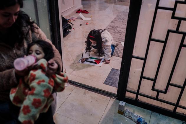 Beirut finishes coloring a Palestinian flag while her mother Neama feeds Fayrouz, at their home in New Cairo, Egypt, on February 29, 2024.