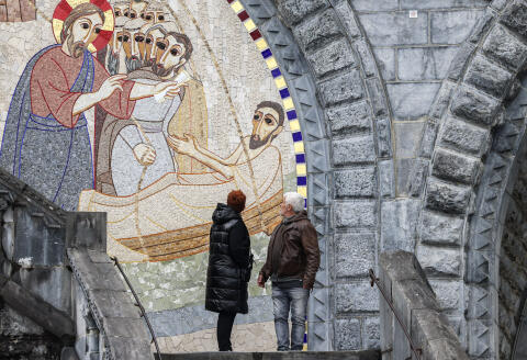 Pedestrians look on to gigantic mosaics, made by artist and priest Marko Rupnik, displayed on the Notre-Dame-du-Rosaire Basilica in the Sanctuary of Lourdes, in Lourdes, southwestern France on March 31, 2023. Reinforced sanctions have been put in place for Rupnik, a Slovenian mosaic artist and a priest who has been "accused and canonically sanctioned for spiritual abuse, psychological abuse and sexual assault", announced the Jesuits' Order of Rome on February 21, 2023. (Photo by Charly TRIBALLEAU / AFP) / RESTRICTED TO EDITORIAL USE - MANDATORY MENTION OF THE ARTIST UPON PUBLICATION - TO ILLUSTRATE THE EVENT AS SPECIFIED IN THE CAPTION