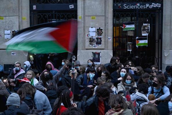 TOPSHOT - A protestor waves a Palestinian flag as they stage a sit-in in front of French riot policemen near the entrance of a Institute of Political Studies (Sciences Po Paris) building occupied by students, in Paris on April 26, 2024. Students occupied a new building at Sciences Po Paris, in support of Palestinians, a day after police evacuated another of the school's sites, echoing protest action at American universities. (Photo by JULIEN DE ROSA / AFP)