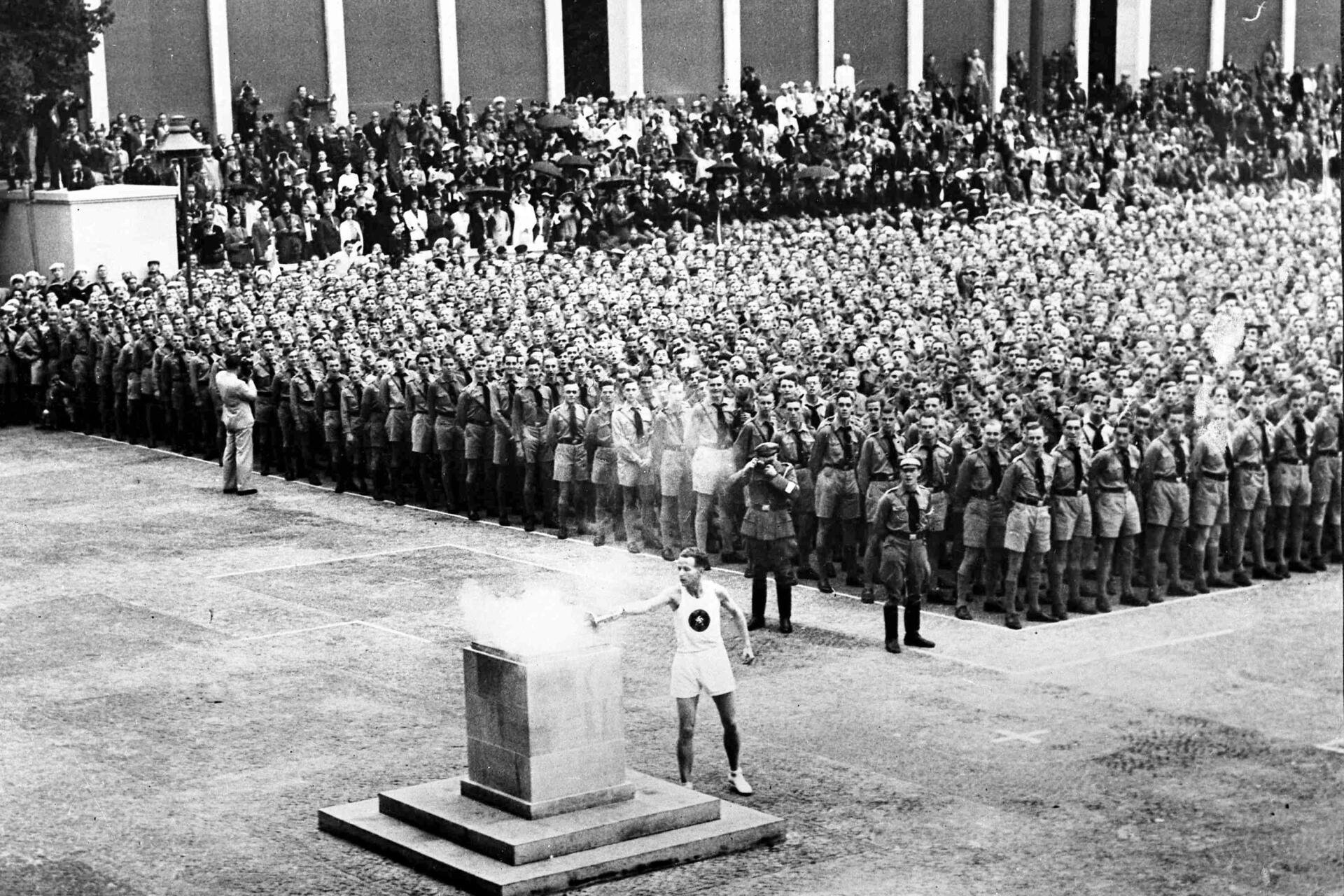 La flamme olympique arrive au Lustgarten de Berlin, le 1ᵉʳ août 1936, sous l’œil des Jeunesses hitlériennes,  après s’être élancée pour la première fois d’Athènes, le 30 juillet 1936.