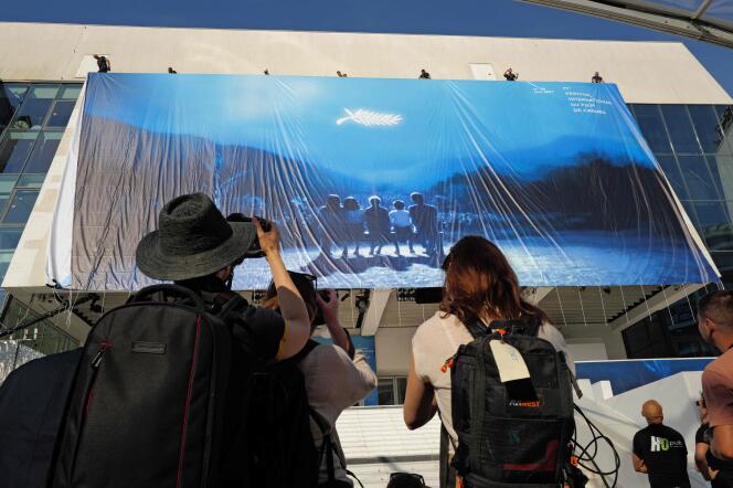 La gente toma fotografías mientras los trabajadores cuelgan el cartel oficial del 77º Festival de Cine de Cannes en la fachada del Palacio de Festivales, en Cannes, el 12 de mayo de 2024. 