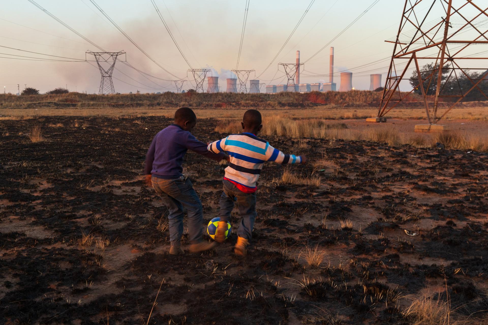 Deux frères, âgés de 10 et 7 ans, jouent à côté de la centrale électrique de Duvha, à Mpumalanga (Afrique du Sud), le 23 juin 2019. Ils vivent sous de grands câbles électriques mais n’ont accès ni à l’électricité ni à l’eau potable.