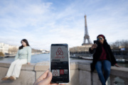 Une femme tient son téléphone portable avec l’application Airbnb tandis que d’autres posent devant la Tour Eiffel, à Paris le 2 février 2024.
