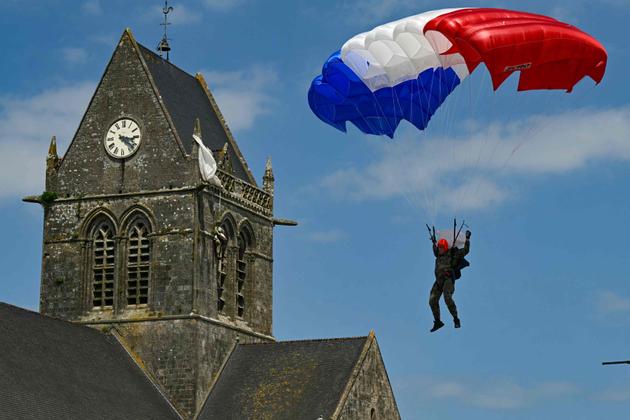 A French Marine Commando paratrooper guides his red, white and blue parachute canopy past the church of Sainte-Mere-Eglise, where a mannequin effigy of WWII veteran US Army 82nd Airborne paratrooper John Steele hangs from the steeple, in Sainte-Mere-Eglise northwestern France, on June 5, 2024.