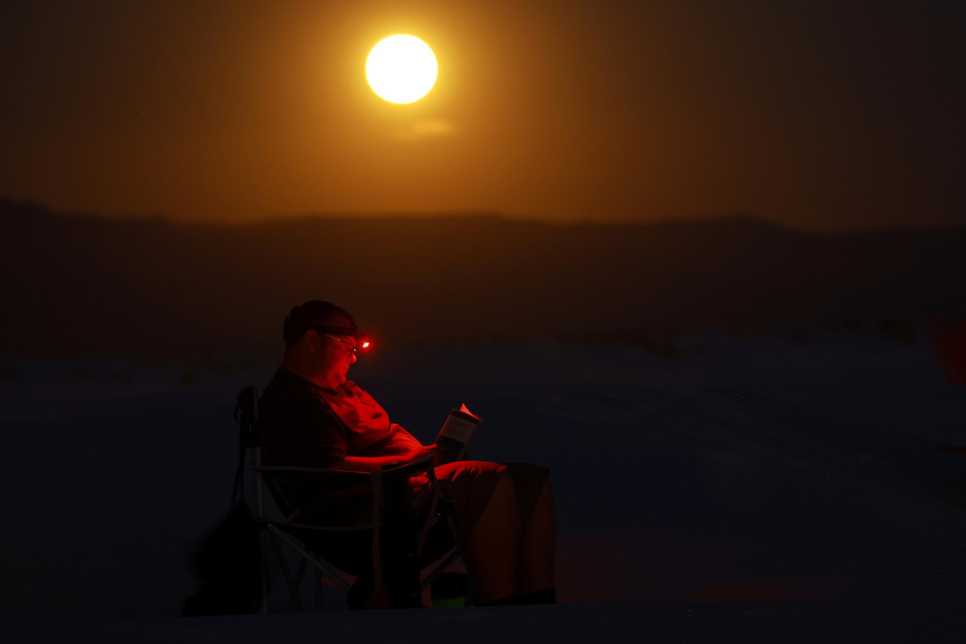 Un uomo legge mentre appare la superluna nel Parco nazionale di White Sands vicino ad Alamogordo, Nuovo Messico, Stati Uniti, 19 agosto 2024. 