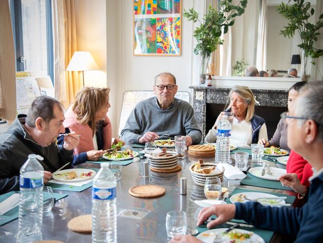 2024 年 5 月 15 日,图尔宽的 Maison d'à côté 大客厅里,人们准备和分享餐点。从左到右依次为 Olivier(住户)、Caroline Bonduelle(Fraternative 联合创始人)、Arnaud(住户)、Bénédicte(来看望她的儿子 Géryck)、Sadia Bourabaa(房屋协调员)和 Gérick(住户)。