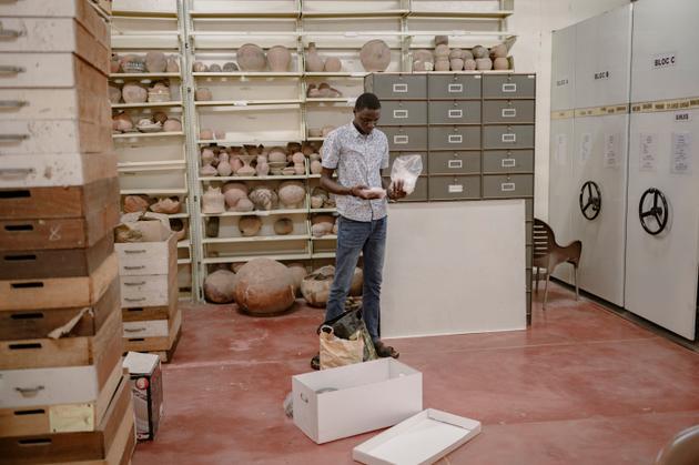 Le doctorant en archéologie René Ndiana Faye, spécialiste de l’histoire de la traite des esclaves, examine des artefacts trouvés sur l’île de Gorée, au large de Dakar, et entreposés à l’Institut fondamental d’Afrique noire, à Dakar, en septembre.