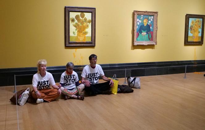 Trois activistes assis devant les « Tournesols » de Vincent van Gogh après avoir jeté de la soupe à la tomate sur deux tableaux de la National Gallery dans le centre de Londres le 27 septembre 2024, suite à la condamnation de leurs collègues activistes Phoebe Plummer et Anna Holland plus tôt dans la journée.
