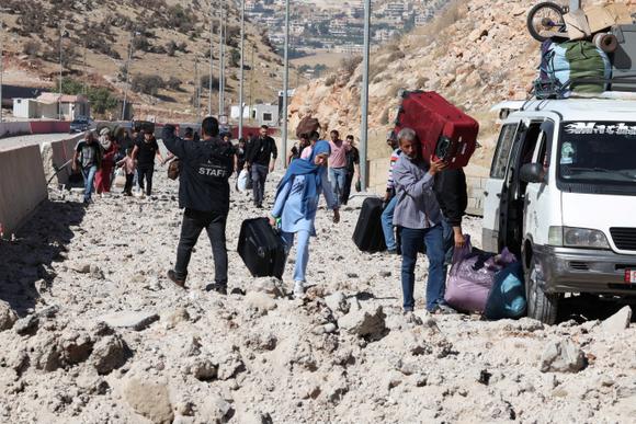 Des personnes transportent leurs affaires en marchant sur les décombres, sur le poste-frontière de Masnaa qui relie la Syrie au Liban, le 4 octobre 2024.