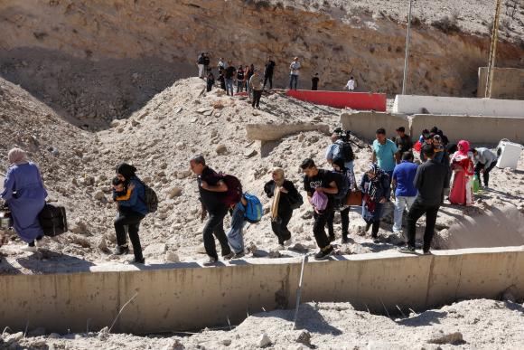 Des personnes marchent sur les décombres, après une frappe israélienne sur le poste-frontière de Masnaa qui relie la Syrie au Liban, le 4 octobre 2024.