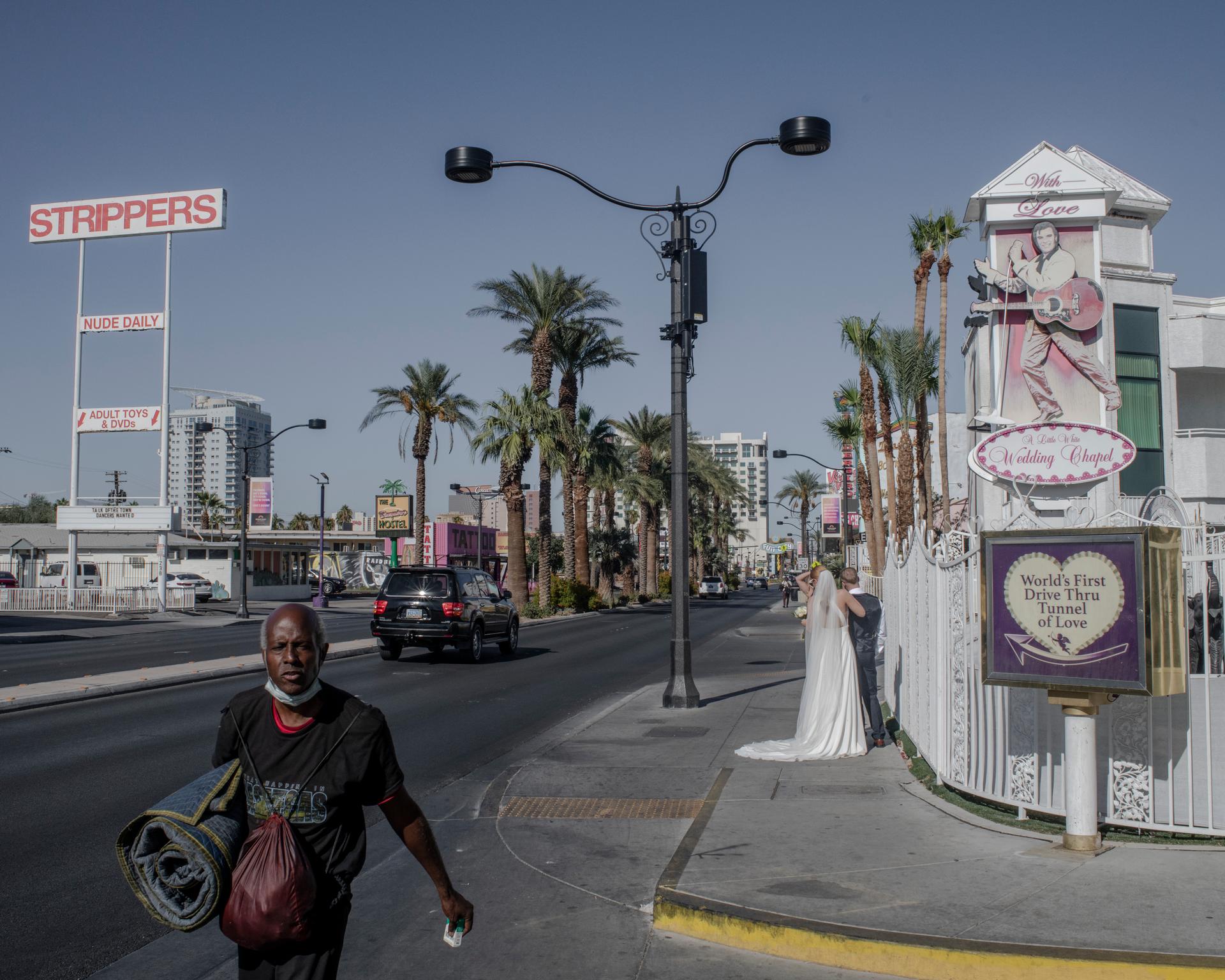 A homeless man walks past a couple just married in the Little White Wedding Chapel, Las Vegas, Nevada, October 9, 2024.