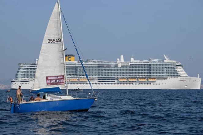 Des militants du collectif Stop Croisières arborent une banderole sur un voilier pour protester contre les bateaux de croisière, alors que le « Costa Toscana » (au second plan) quitte le port de Marseille, dans le sud de la France, le 17 juin 2023.