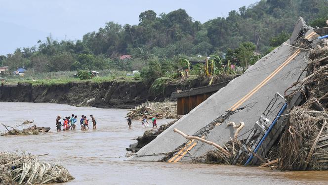 Des personnes traversent une rivière près d’un pont qui s’est effondré après que la rivière a débordé en raison des fortes pluies provoquées par la tempête tropicale Trami, à Laurel, dans la province de Batangas, au sud de Manille, le 25 octobre 2024. 