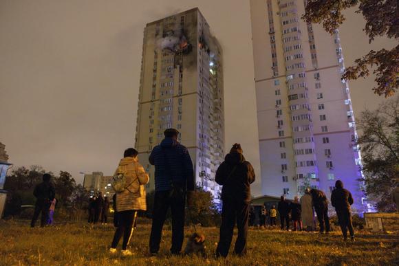 Des personnes regardent un immeuble qui a été touché par un drone russe, à Kiev, vendredi 25 octobre 2024 au soir.