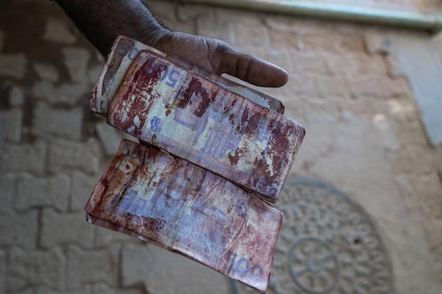 A man pulls bloodstained banknotes out of his pocket in the courtyard of Al-Naw Hospital, Omdurman, Sudan, October 29, 2024. He was drinking tea with his family in Bahri, north of Khartoum, when they were blown up by artillery fire. One teenager was killed instantly, while a dozen others were injured.