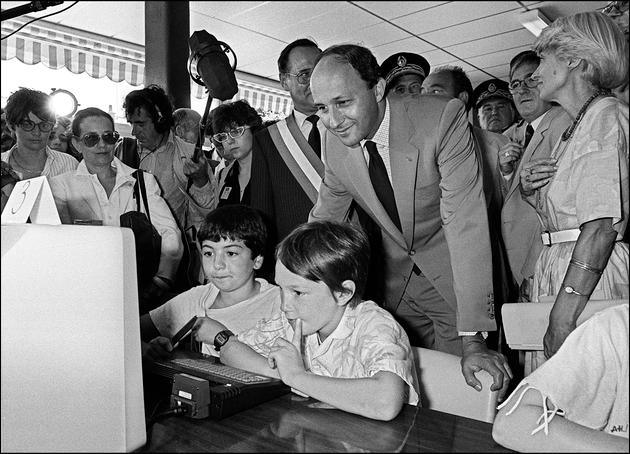 Le premier ministre Laurent Fabius suit les démonstrations sur un ordinateur de deux jeunes élèves du groupe scolaire Henry-Pellet à Langeais (Indre-et-Loire), le 19 juillet 1985, lors d’une étape de son tour de France pour la mise en œuvre du plan Informatique pour tous.