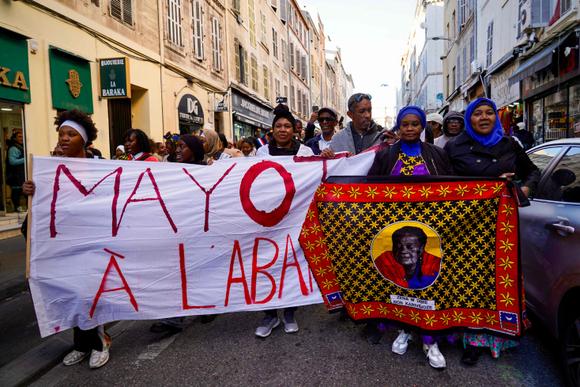 Manifestantes, com uma faixa denunciando “Mayotte Abandonada” e uma bandeira com um retrato da política francesa Zena M'Dere, durante uma manifestação de apoio aos habitantes de Mayotte, em Marselha, 21 de dezembro de 2024.
