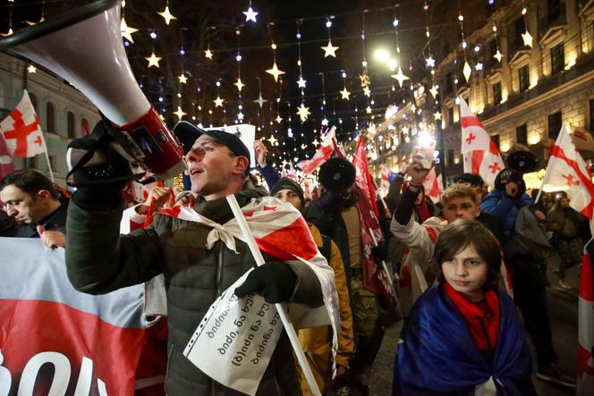 Manifestantes carregando bandeiras da Geórgia marcham durante uma manifestação antigovernamental em frente ao prédio do Parlamento em Tbilisi, Geórgia, sábado, 28 de dezembro de 2024.