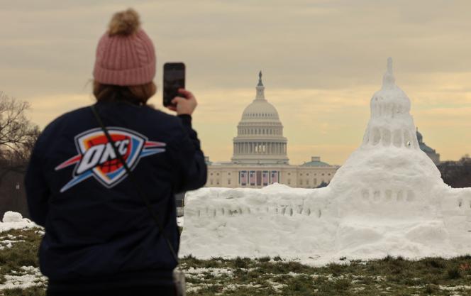 Une touriste prend une photo d’une sculpture de neige représentant le Capitole des États-Unis avec le Capitole en arrière-plan, paré de drapeaux pour l’investiture de Donald Trump, sur le National Mall, à Washington DC, le 13 janvier 2025.