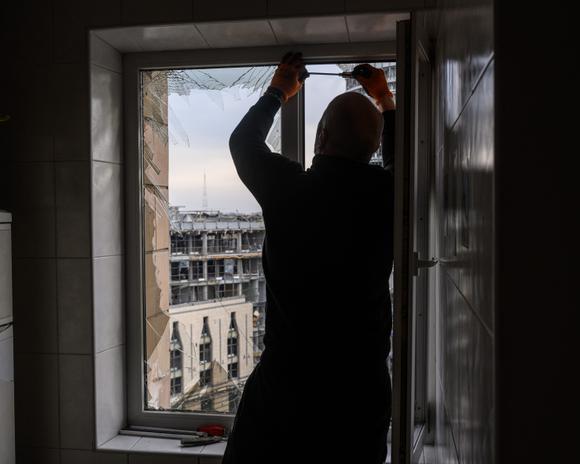 Une personne pose une bâche en plastique sur une fenêtre d’un immeuble après l’attaque russe sur le quartier de Lukianivka dans le centre de Kiev, le 18 janvier 2025.