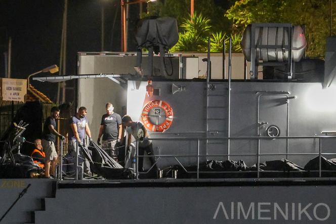 Des hommes transfèrent les sacs mortuaires des migrants décédés, après le chavirement de leur bateau en pleine mer au large de la Grèce, à bord d’un navire des garde-côtes dans le port de Kalamata, en Grèce, le 14 juin 2023. 