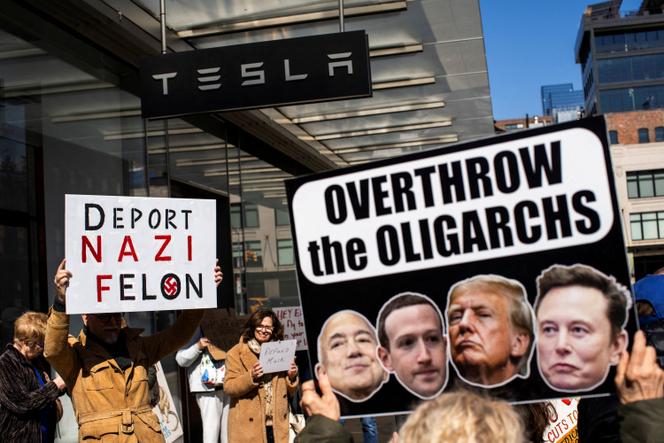 Lors d’une manifestation devant une enseigne Tesla, à New York, le 1ᵉʳ mars 2025. Sur les pancartes, on peut lire « Expulsez le criminel nazi » et « Renversez les oligarques ».