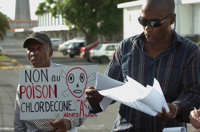 L’avocat Harry Durimel (à droite) et un militant portant une pancarte « Non au poison chlordécone » manifestent à l’arrivée de la ministre de la santé, Roselyne Bachelot, aux Abymes, à la Guadeloupe, le 18 novembre 2007.