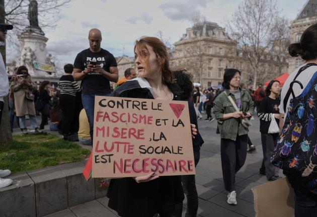 A woman holds a placard reading "Against fascism and misery, social struggle is necessary" as she walks as part of the international day against racism and fascism, in Paris, on March 22, 2025. 