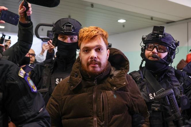 Mohamed Amra escorté par des policiers, à l’aéroport de Bucarest, le 25 février 2025.