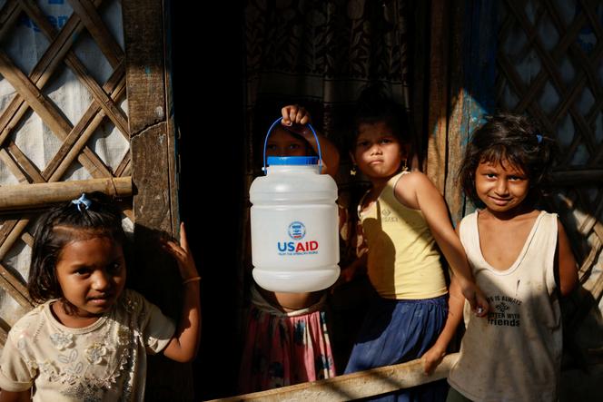 Réfugiés Rohingya tenant une jarre siglée du logo Usaid, dans le camp de Cox’s Bazar, au Bangladesh, le 16 mars 2025.