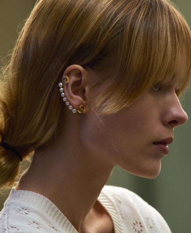 Monoboucle d’oreille Menottes, en or jaune et perles, Dinh Van, 1 990 €. Pull Eric Bompard.