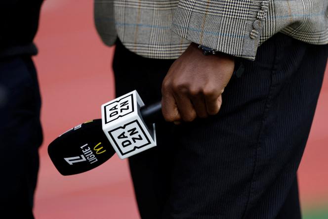 Un commentateur tient un micro DAZN avant le match de Ligue 1 entre l’AS Monaco et le RC Strasbourg, au stade Louis-II, à Monaco, le 19 avril 2025.