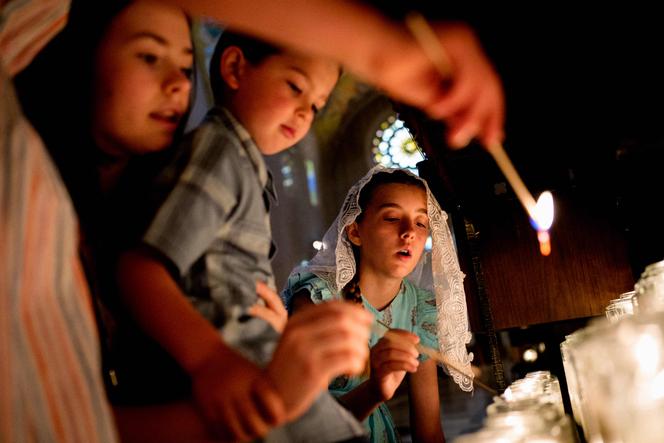 Une gardienne de paroisse et des enfants allument des bougies votives dans la basilique du sanctuaire national de l’Immaculée Conception, à la suite du décès du pape François, le 21 avril 2025, à Washington.