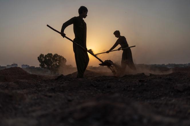 Shaidullah, 15 ans, et Jangvir, 16 ans, enlèvent la terre du dessus des briques pour les laisser refroidir avant de les extraire, après leur cuisson dans un four pendant une vague de chaleur à Islamabad, au Pakistan, le 16 mai 2025.