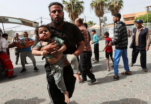 Un homme porte un enfant blessé à l’hôpital des martyrs d’Al-Aqsa après une frappe israélienne, à Deir Al-Balah, dans le centre de la bande de Gaza, samedi 17 mai 2025.