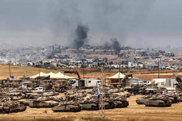 Des chars et des bulldozers israéliens déployés à la frontière avec la bande de Gaza, alors que de la fumée s’élève au-dessus des bâtiments détruits à Gaza lors d’un bombardement israélien, le 17 mai 2025.