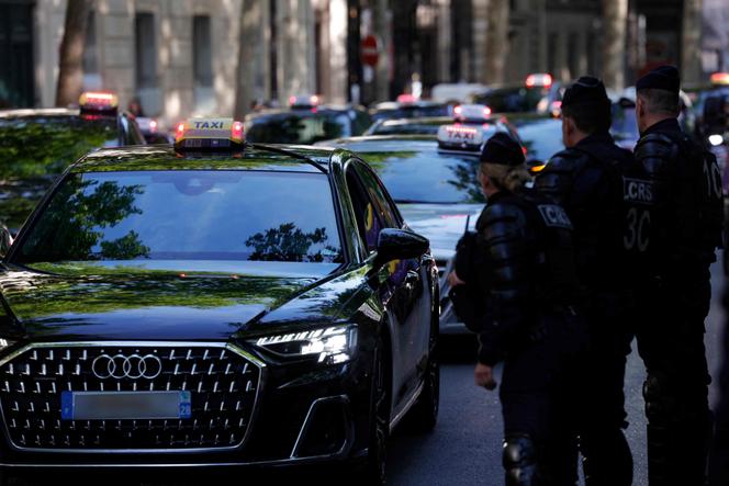 Des policiers antiémeute montent la garde alors que des taxis se rassemblent dans une rue de Paris, le 19 mai 2025.