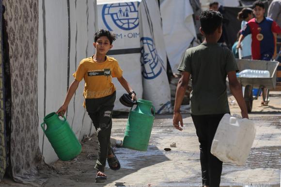 Un jeune Palestinien court vers un camion-citerne chargé d’eau, dans le camp de réfugiés de Nousseirat, dans le centre de la bande de Gaza, le 24 mai 2025.