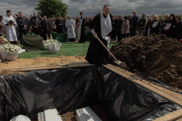 Un prêtre ukrainien jette des pelletées de terre sur les cercueils de Roman Martyniuk, 17 ans, de sa sœur Tamara, 11 ans, et de son frère Stanislav, 8 ans, tués dans une frappe d’un missile russe, dans un cimetière de Korostychiv, le 28 mai 2025.